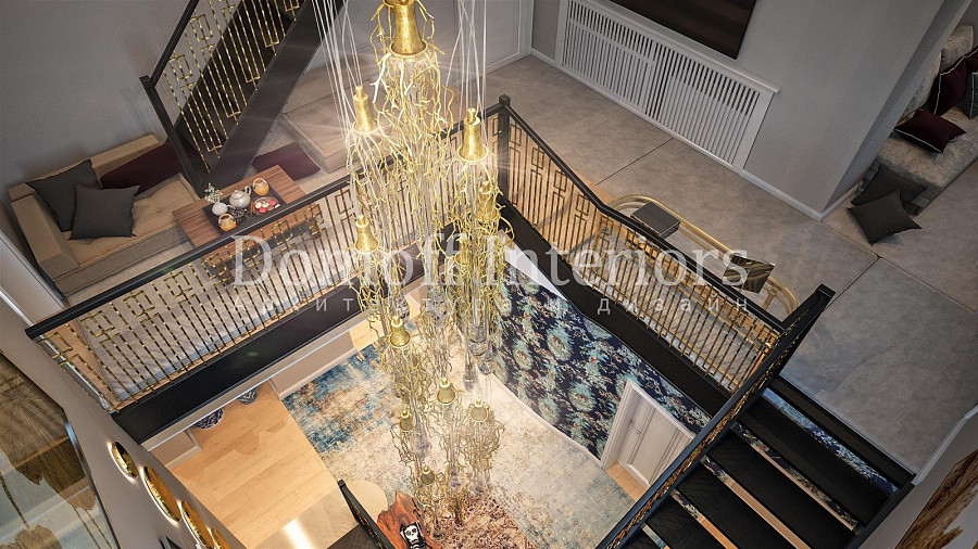 Длинная золотая эко-люстра в виде колокольчиков ниспадает вдоль лестницы от потолка верхнего этажа до входного холла в загородном доме
